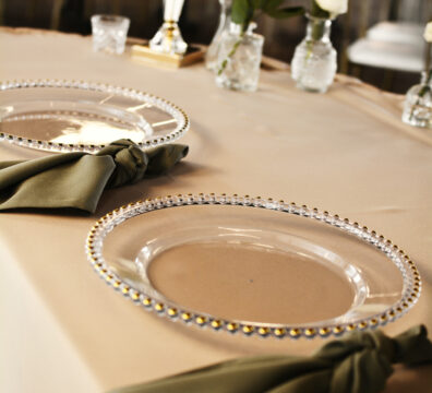 beżowe obrusy na stoliki dla gości, podtalerze ze złotymi brzegami, serwety materiałowe