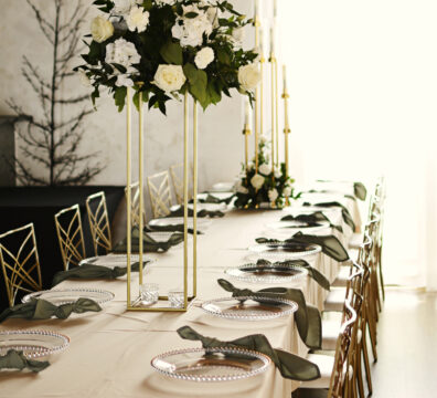 dekoracja weselna, beżowe obrusy, serwety szałwiowe, podtalerze akrylowe ze złotymi brzegami, stojaki geometryczny z bukietem z róż