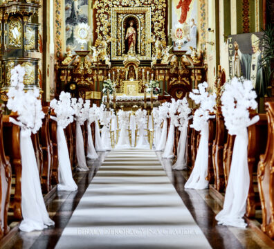 dekoracja ławek tkaniną i gałązkami z kwiatów wiśni, krzesła złote z dekoracją z kwiatów i biały dywan na ślub