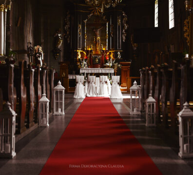 dekoracja ślubna z czerwonym dywanem, białymi latarniami i złotymi krzesłami z czerwoną różą