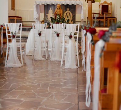 Bordowa dekoracja kościoła na ślub. Białe krzesła chiavari